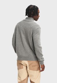 Szary dzianinowy sweter z zagiętym kołnierzem, prążkowanymi mankietami i dołem. Noszony z jasnobeżowymi spodniami z dwoma wyraźnymi kieszeniami.