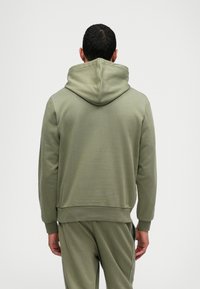 Ελιά χρώματος  φούτερ με κουκούλα, ραμμένα μανίκια και ζώνη. Λείο υφασμα, εφαρμοστή γραμμή, και η πίσω όψη δείχνει ραφές λεπτομέρειας.