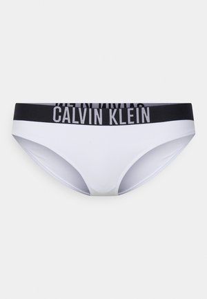 Bijeli donji dio bikinija napravljen od glatkog materijala, s crnim elastičnim pojasom na kojem je logo "CALVIN KLEIN". Klasičan kroj s minimalnom pokrivenošću.