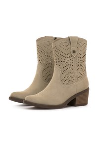 Botas de tobillo de ante beige con detalles recortados, punta afilada y tacón apilado. Presenta adornos de costura y cierre con cremallera lateral.