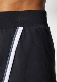 Svarte trening-shorts med bred elastisk midje og vertikale hvite sidebånd på hvert ben, laget av mykt bomullsmateriale.