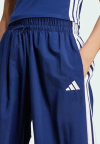 Marineblaue Sporthosen mit elastischem Bund, weißen seitlichen Streifen und einem gestickten weißen Logo. Der Stoff wirkt weich und strapazierfähig.