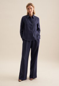 Chemise en lin bleu marine avec un col et des boutons à l'avant, associée à un pantalon ample assorti. Design simple et texture légère.