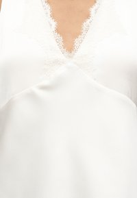 Λευκό αμάνικο ένδυμα με V-λάστιχο, διακοσμημένο με λεπτή δαντέλα στην περιοχή του στήθους.