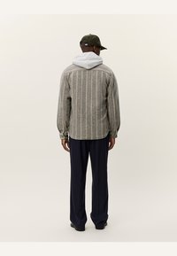 Gray striped shirt with a white hoodie underneath, paired with navy pants. Features long sleeves and a relaxed fit. Back view shown.