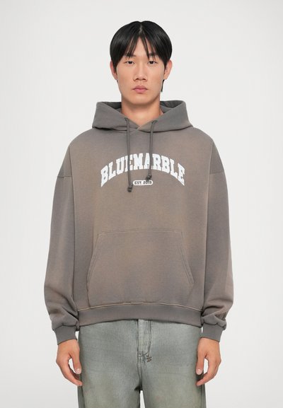 Sudadera gris con bolsillo frontal y capucha ajustable; presenta el texto blanco "BLUemarble EST. 2019" en el pecho. Tejido suave, corte relajado.