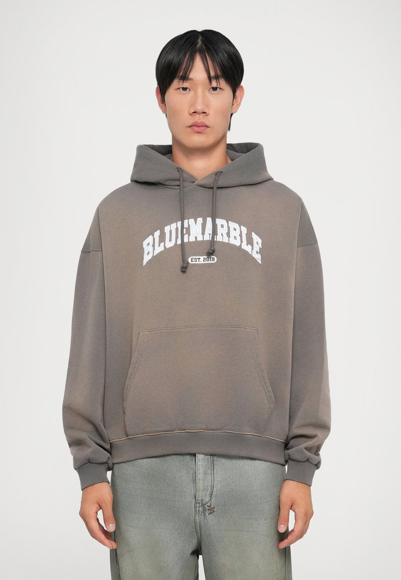 Sweatshirt gris avec une poche avant et une capuche à cordon ; présente le texte blanc "BLUemarble EST. 2019" sur la poitrine. Tissu doux, coupe décontractée.