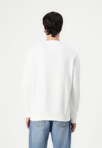Hvit genser med lange ermer, ripset mansjetter og hem, samt en V-søm detalj bak. Kombinert med lys blå løse jeans.