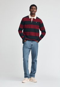 Langärmliges Poloshirt mit roten und schwarzen Streifen, beiger Kragen, kombiniert mit hellblauen Jeans und cremefarbenen Sneakers. Einfaches Design, lässige Passform.