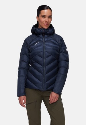 Marineblaues Daunenjacke mit einem Chevron-Muster, Kapuze, Reißverschluss und Logodetail auf der Brust. Der Stoff wirkt glatt und glänzend.