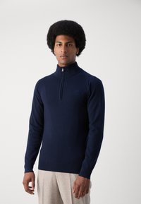 Suéter de punto azul marino con un cuello alto y una cremallera de cuarto. Presenta puños y bajo acanalados, elaborado con una tela suave y lisa.