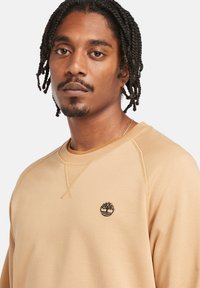 Beige sweatshirt med rund halsudskæring, ribbede manchetter og broderet logo på brystet, med en glat tekstur og klassisk pasform.
