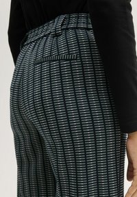 Zwart-wit gestreepte broek met een strakke tailleband, voorzien van een achterzak en een gestructureerd, verticaal streeppatroon.