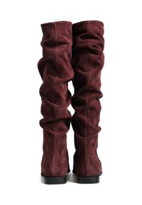 Burgundowe kozaki za kolano wykonane z miękkiego zamszu. Cechują się luźnym fasonem, teksturowanym materiałem i niskim czarnym obcasem.