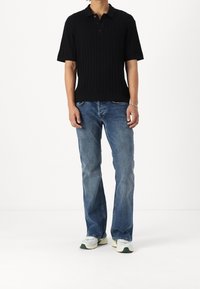 Camisa polo negra con canales y mangas cortas, combinada con jeans azul de corte relajado y zapatillas ligeras con acentos verdes.