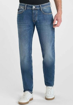 Jeans de mezclilla azul con un corte recto, lavado medio, diseño de cinco bolsillos y costuras contrastantes; combinados con zapatillas blancas.