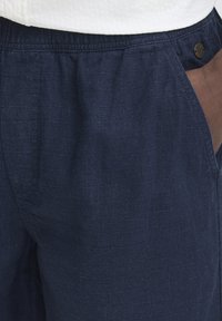 Ľanové nohavice námorníckej modrej farby s textúrovanou látkou, elastickým pásom a bočnými vreckami, s jemným logom na páse.
