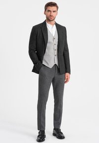 Giacca di suit grigia in lana sopra un gilet grigio chiaro, abbinata a pantaloni grigi. Stile con una camicia bianca e scarpe di pelle nere.