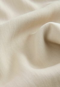 Tissu doux de couleur crème avec une texture tissée fine et des plis délicats créant des ombres et des reflets lisses.