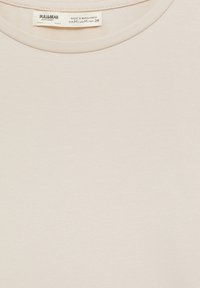 Vaalea beige puuvillapaita, jossa on pyöreä kaula-aukko ja hienovarainen pinnan rakenne. Etiketissä lukee brändi Pull&Bear ja koko M.