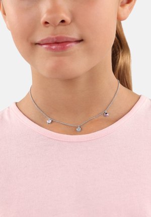 Silberne Kettenhalskette mit drei Anhängern: einem Schmetterling, einer Blume und einem Herz, die jeweils mit bunten Akzenten verziert sind. Tragen über einem pinken Shirt.