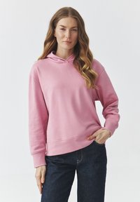 Felpa con cappuccio rosa a maniche lunghe, tessuto morbido, vestibilità comoda, polsini e orlo a costine, abbinata a jeans in denim scuro.
