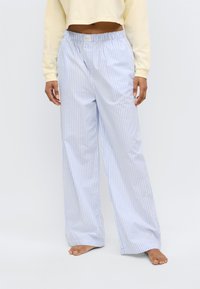 Παντελόνι πιτζάμας με μπλε και λευκές ρίγες, άνετη εφαρμογή, ελαστική μέση και ελαφρύ ύφασμα. Ώριμα πόδια φαίνονται κάτω από το στρίφωμα.