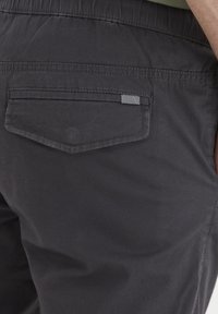 Pantalones de algodón negros con un bolsillo trasero que presenta un acento de raya diagonal. Cintura elástica y textura suave y mate.