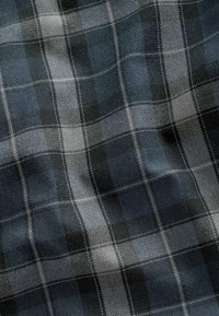 Tissu à carreaux bleu et gris avec une texture tissée, présentant un motif à carreaux de nuances variées et des plis subtils.
