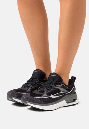 Zapatillas deportivas negras con materiales de malla y ante, que cuentan con una media suela blanca, acentos grises y un collar acolchado para mayor comodidad.