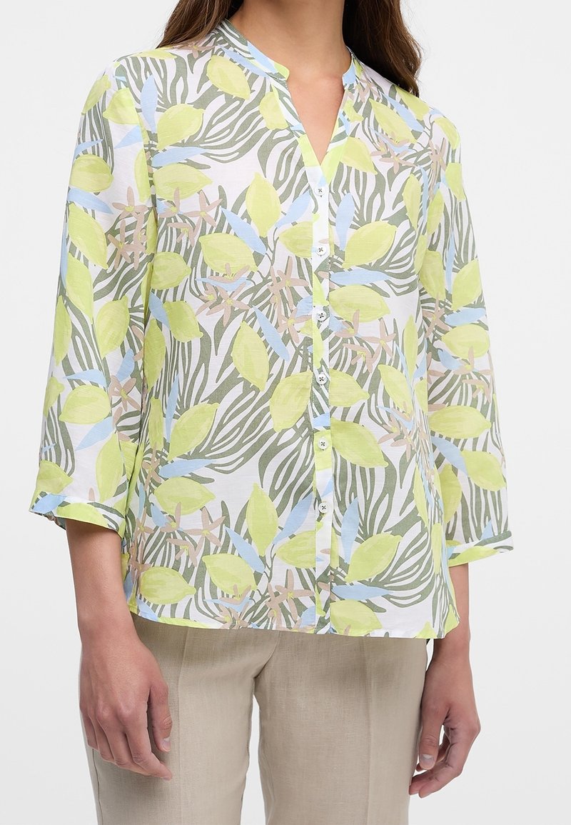 Blouse boutonnée à manches trois-quarts en tissu blanc avec des motifs de feuilles et abstraits verts, bleus et beiges.