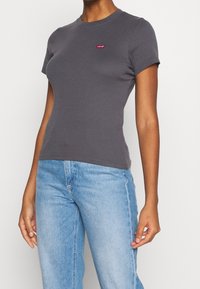Grå bomulds t-shirt med rund hals og korte ærmer, med et lille rødt Levi's logo på brystet. Kombination med lyseblå jeans.