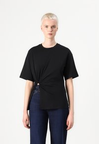 Tricou negru cu mânecă scurtă, având un detaliu legat la talie, realizat dintr-un material moale; asortat cu blugi din denim.