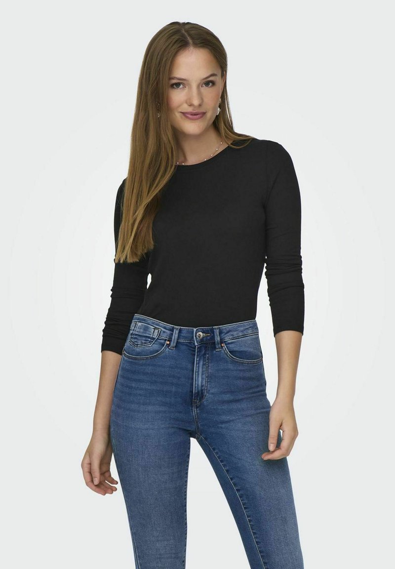 Svart langermet topp med rund hals, kombinert med blå høytlivsjeans som viser en tettsittende design og jevn tekstur.