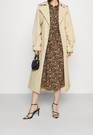 Hellbeige Trenchcoat über einem braunen, leopardgemusterten Kleid mit roten Akzenten. Hat eine taillierte Taille, kurze Ärmel und schwarze Riemchen-Heels.