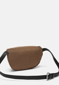 Brun stof-taljeveske med en sort justerbar læderrem og sølvfarvet spænde på en hvid baggrund.