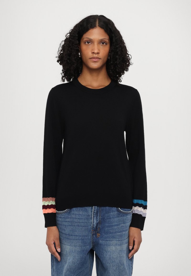 Svart genser med lange ermer, rund halslinje og teksturerte ribbede mansjetter med bølgemønstre i rosa, grønn, blå og lilla.