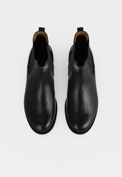 Paire de bottines en cuir noir avec des bouts arrondis et des panneaux latéraux élastiques, vue de dessus sur fond blanc.