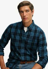 Donkerblauwe en turquoise geblokte overhemd met een kraag, lange mouwen en een zakdetail. Draagt over een wit T-shirt, aangevuld met denim.