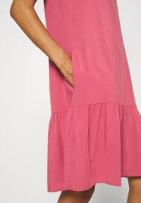 Rotes Kleid mit ausgestellt geschnittenem Saum und Taschen, aus weichem Stoff mit glatter Textur. Das Design ist schlicht und lässig.