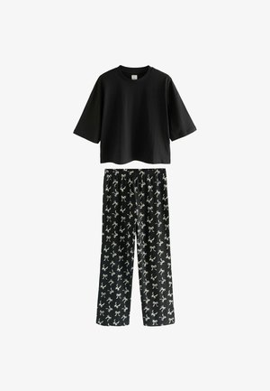 Camiseta de algodón negra con mangas cortas y corte holgado, combinada con pantalones negros que presentan un estampado de lazo blanco, cintura elástica y piernas rectas.