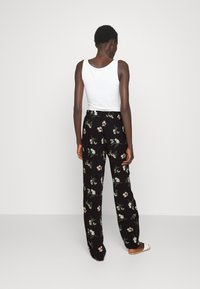 Black floral pants with a loose fit, featuring pink and white flower patterns. Paired with a plain white tank top.