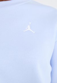 Lys blå hettegenser laget av bomullsblanding. Har en hvit brodert Jumpman-logo på brystet og ribbestrikket hals.