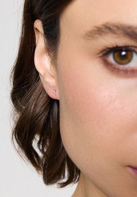 Kolczyk wkręcany wykonany z metalu z przezroczystym kamieniem szlachetnym, o prostym, okrągłym kształcie. Noszony w płatku ucha.