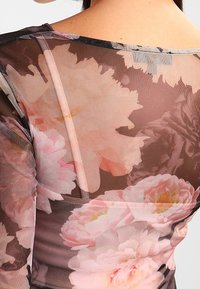 Průhledná síťová halenka s květinovým potiskem v jemných růžových a broskvových odstínech, s kulatým výstřihem a dlouhými rukávy. Texturovaná, lehká tkanina.