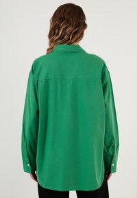 Green, long-sleeve shirt with a collared neck, relaxed fit, and button cuffs. Features a back yoke seam. Made from a smooth fabric.
