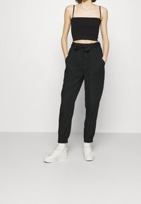 Svart kortärmad top i crop-modell tillsammans med svarta byxor med dragsko, som har sidofickor och elastiska mudd. Outfitten kompletteras med vita sneakers.