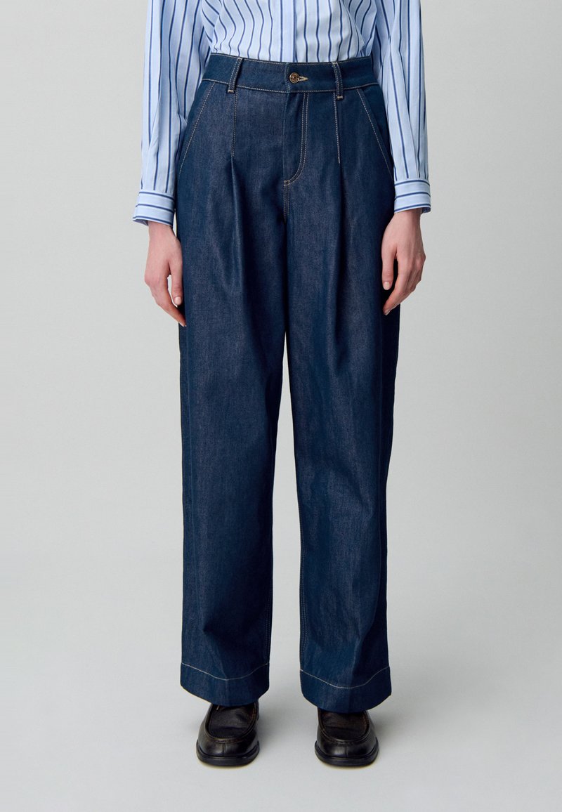 Pantalones de mezclilla oscura de pierna ancha con talle alto, que presentan costuras en contraste y un detalle de botón en la cintura.