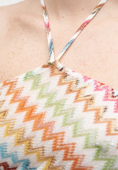 Κοντινό πλάνο ενός halter neck με λεπτές, πολύχρωμες ζιγκ ζαγκ τιράντες και αντίστοιχο υφή ύφασμα πάνω σε γυμνό δέρμα.
