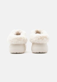 Fehér, szőrmebéléssel ellátott faalj, lekerekített háttal, texturált gumitalppal és oldalán "crocs" logóval. Puha, bolyhos felső anyag.